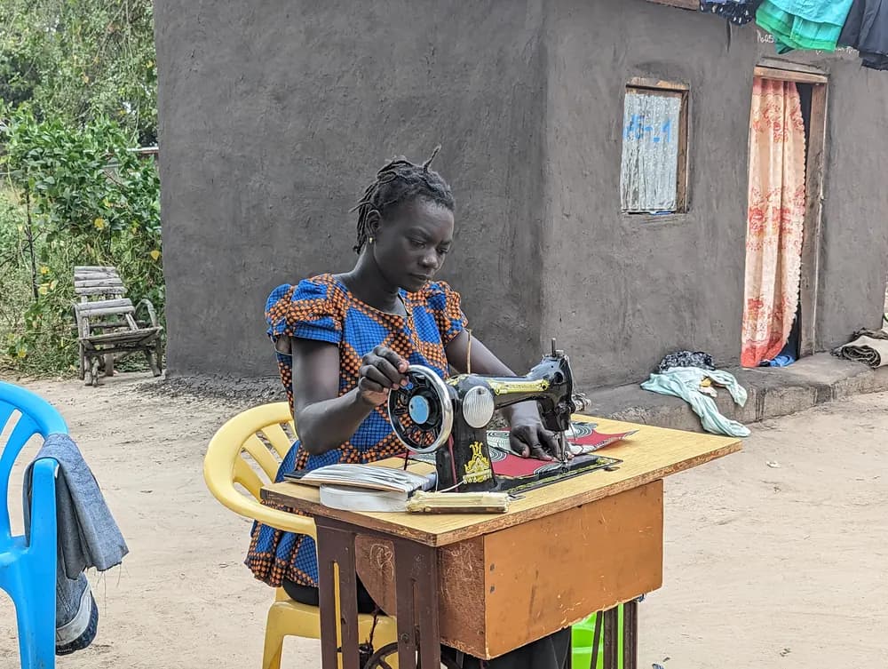 A tailor at her sewing machine outside her home