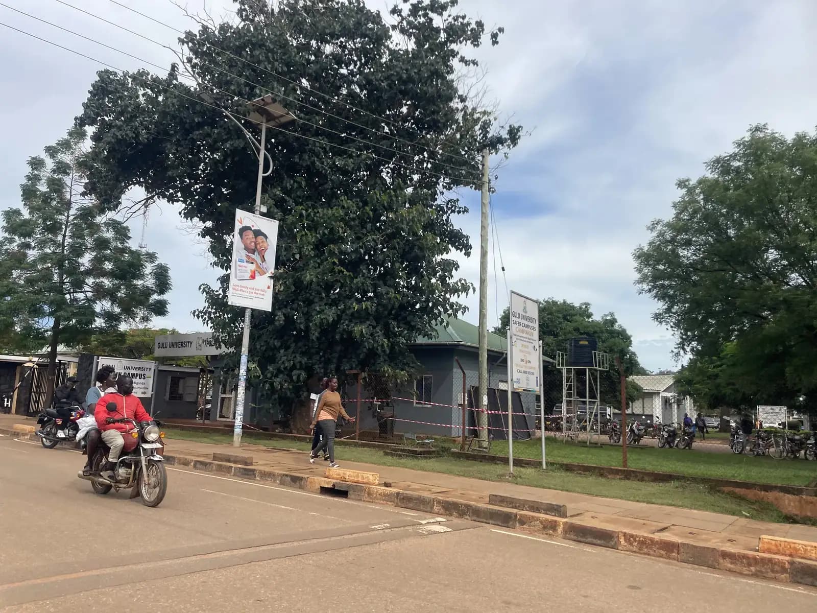 A boda boda rider on a tree-lined road near Gulu University